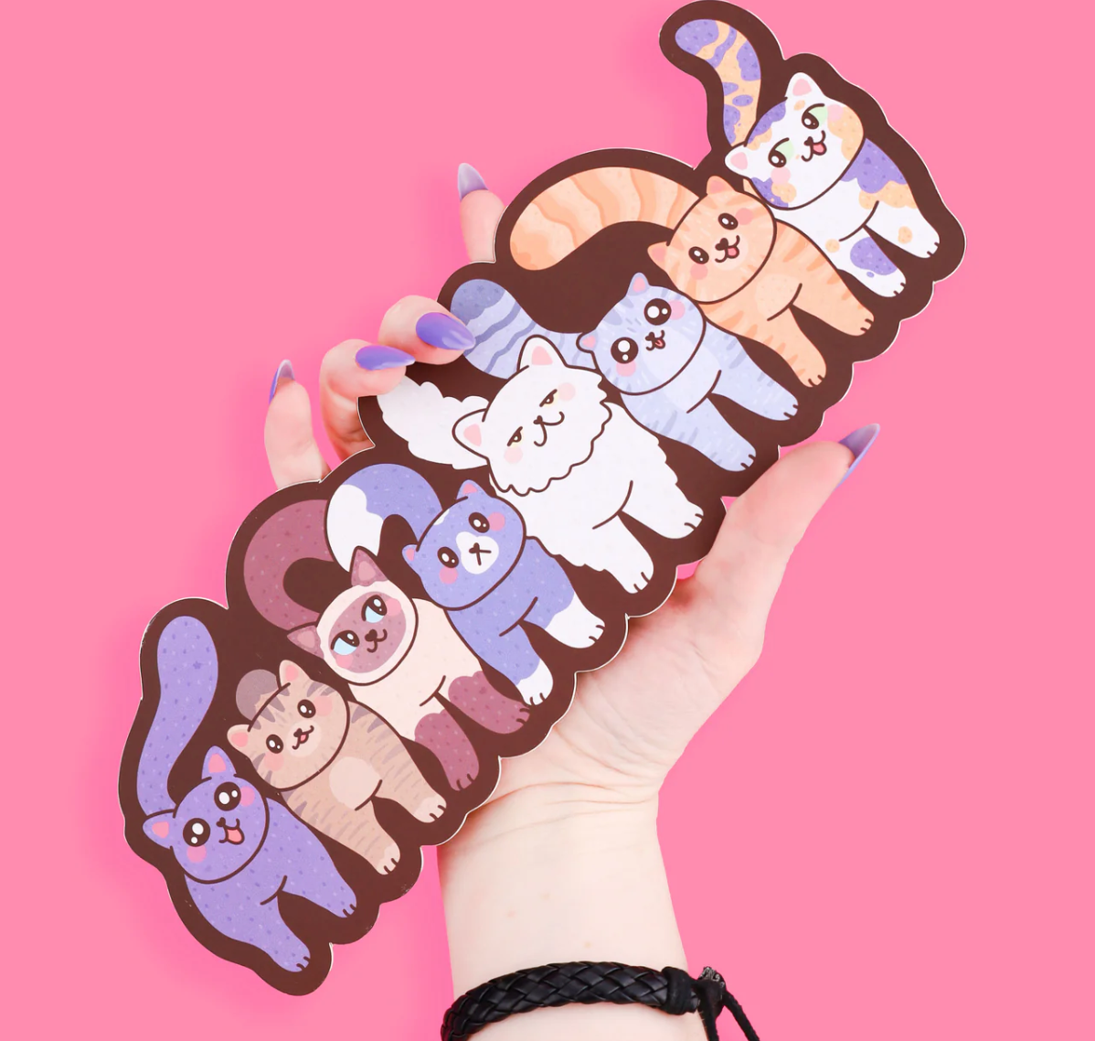 Funny Cats Bookmark featuring a row of colorful cartoon cats, held against a pink background.