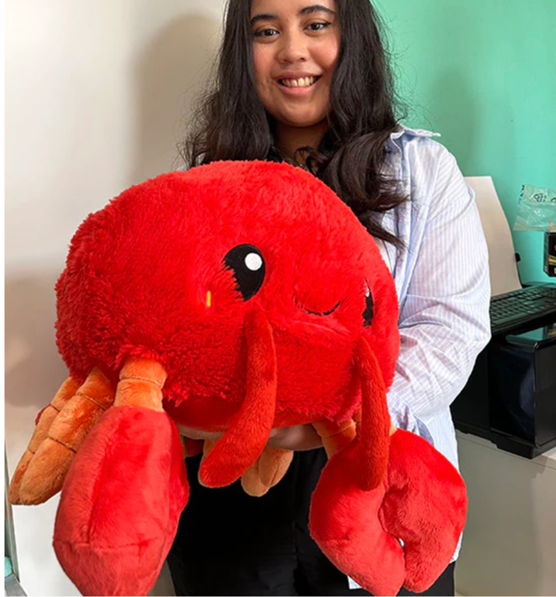 Person holding a large, bright red, plush Lobster toy with friendly eyes and claws.