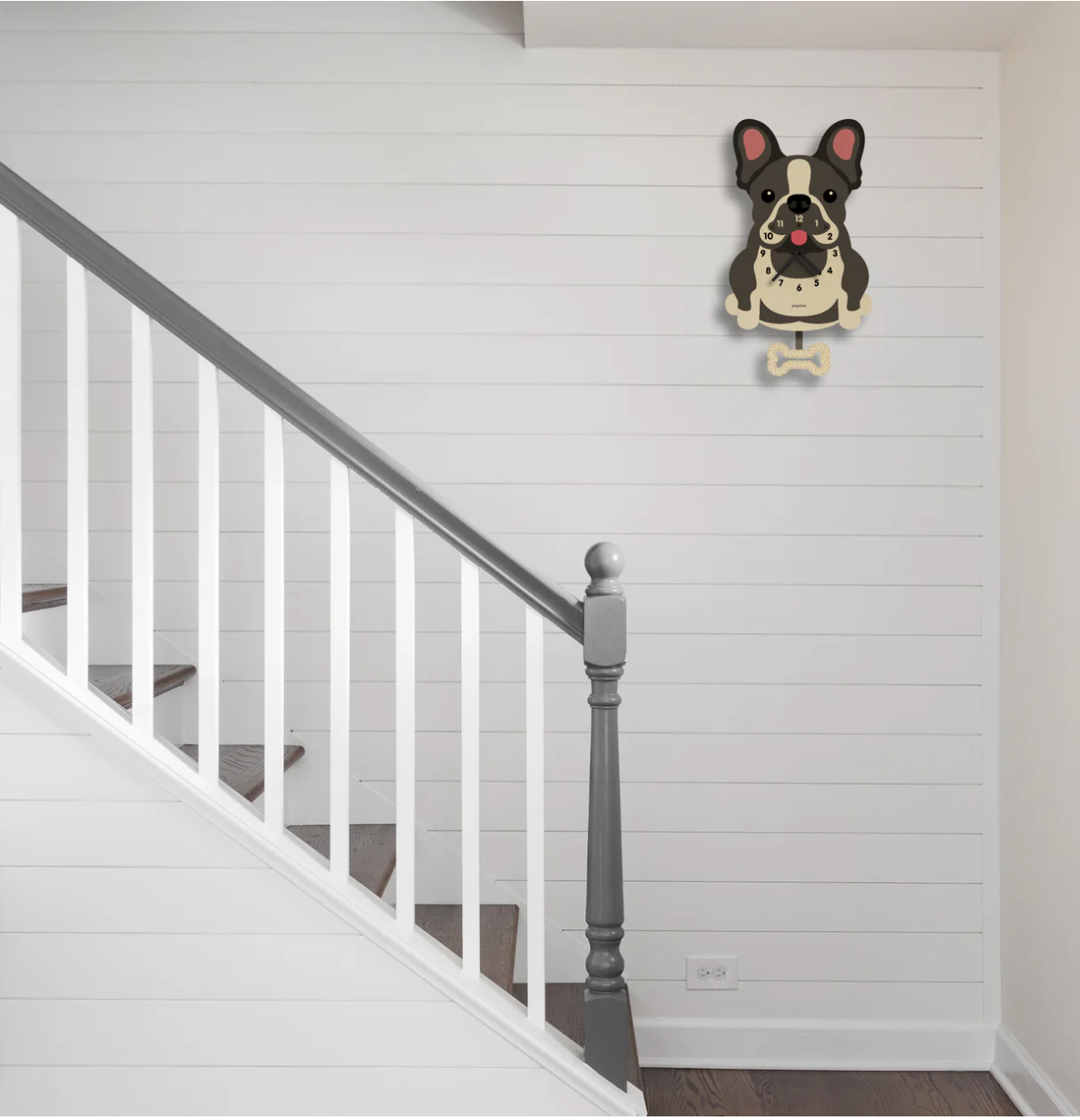 Wood Pendulum Clock | French Bulldog hanging on white wall next to staircase with swinging bone pendulum.