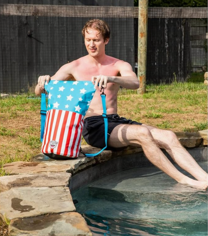 Man sitting by pool holding Dry Bag | Americana with stars and stripes waterproof design and backpack straps.