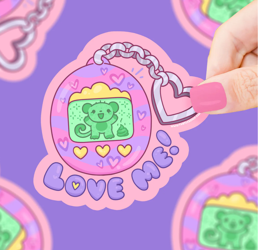 Love Me Virtual Pet Sticker showing a cute green virtual pet with hearts and a pink heart charm keychain.