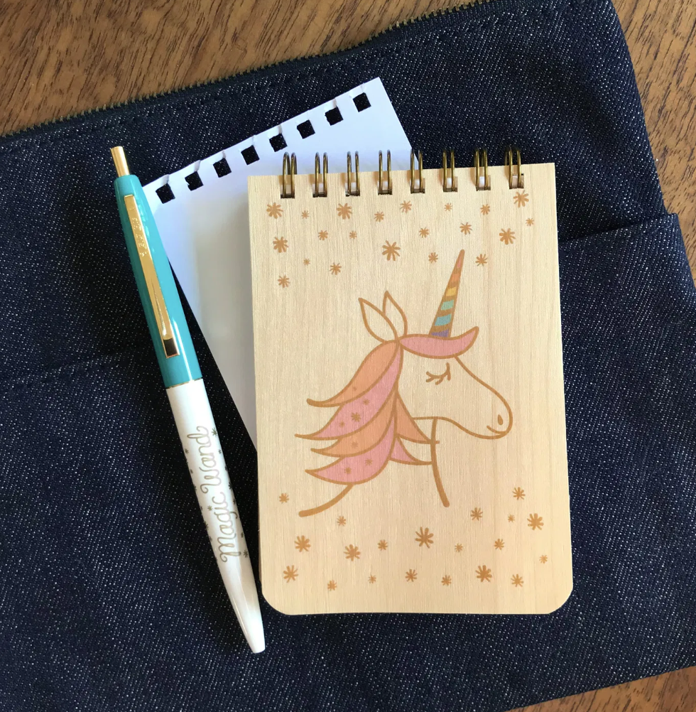 Mini Wood Notebook | Magical Unicorn with spiral binding and unicorn design, paired with a pen on dark fabric background.