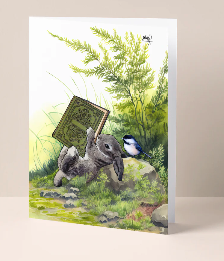 Turn The Page Bunny Card features a rabbit holding a book amid green foliage, blank inside, FSC certified paper.