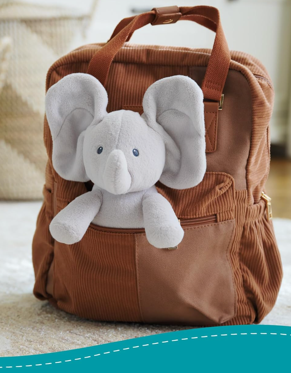 Peek-a-Boo Flappy the Elephant soft gray plush toy with large ears sitting in brown backpack pocket.