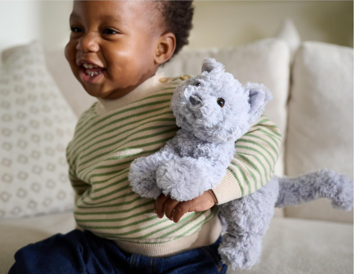 Child smiling and holding a plush gray cat toy in a pounce pose, Bootsie English Blue Kitten.