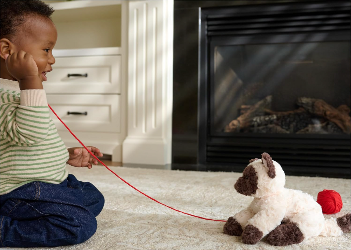 Bootsie Siamese Kitten plush with cream and chestnut fur and bright blue eyes beside a child playing indoors.