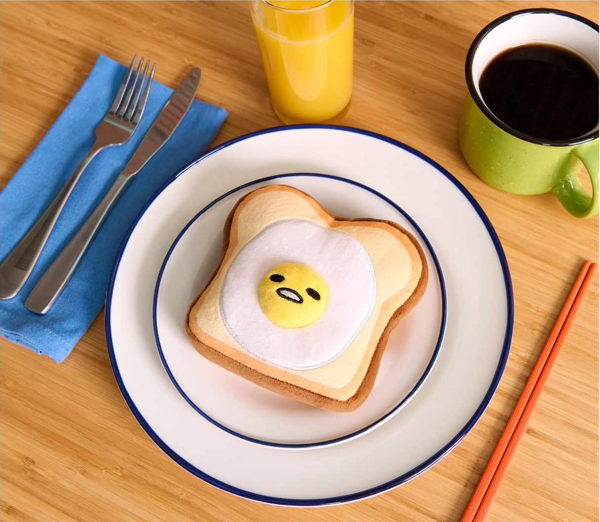 Gudetama Egg Toast plush on a plate with fork, knife, orange juice, and coffee on a wooden table.