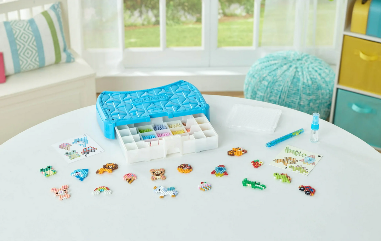 Aquabeads Beginners Craft Studio with colorful bead designs, flip tray, sprayer, double-sided pen, and storage case on table.