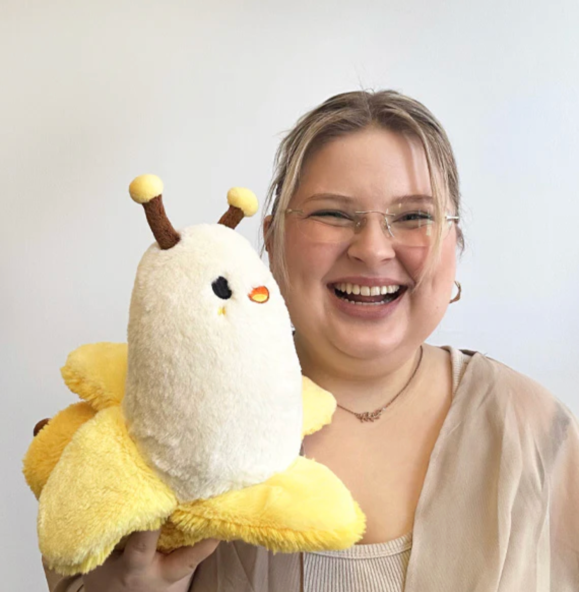 Happy woman holding a soft, plush Banana Slug Mini toy with yellow and white colors and cute antennae.