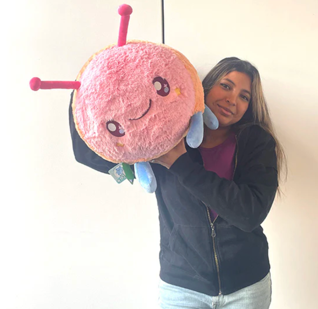 Person holding a large pink Rainbow Caterpillar Mega plush toy with smiling face and antennae.