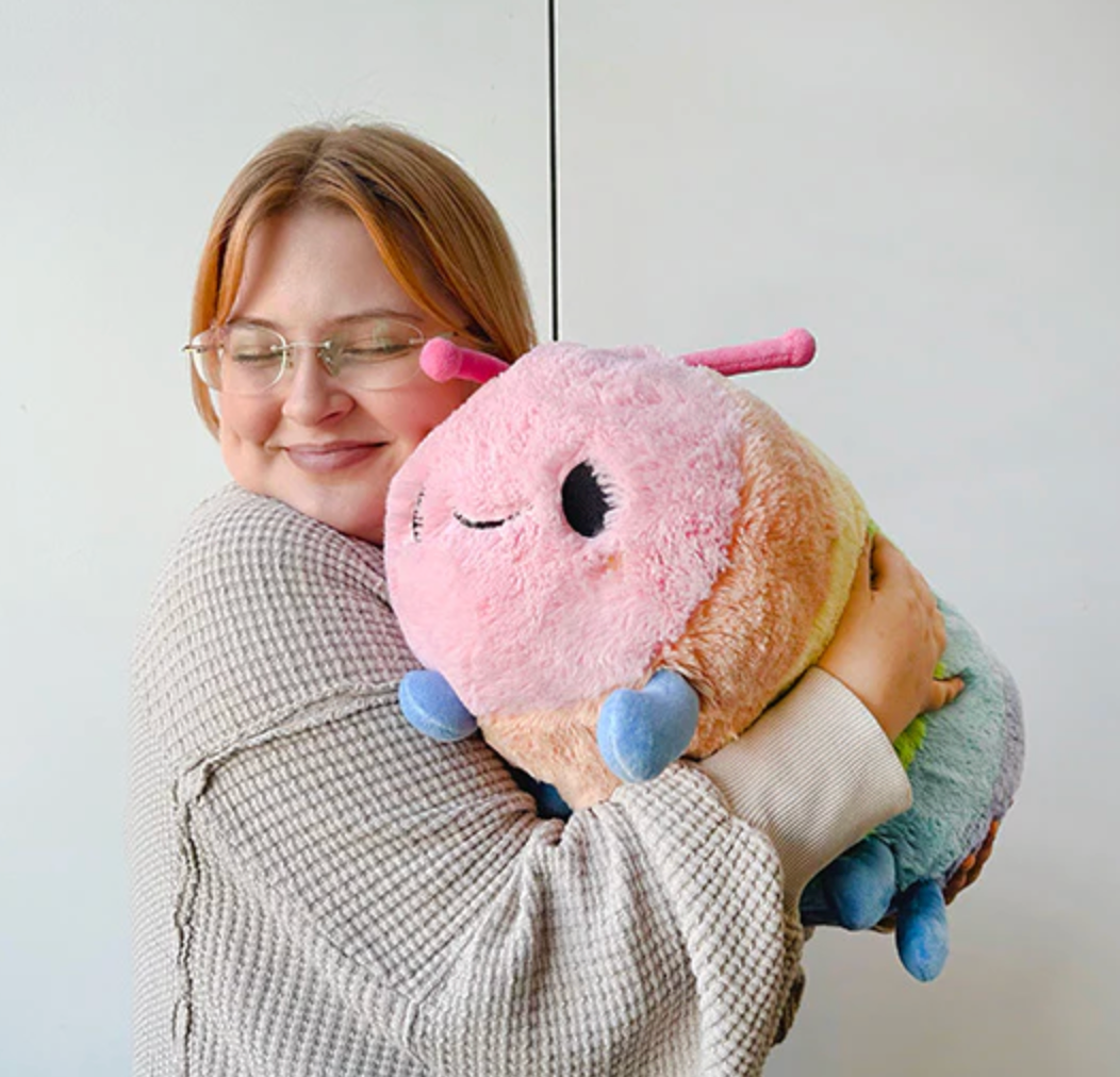 A woman happily hugging a soft, colorful plush toy called the Rainbow Caterpillar, perfect for all ages.
