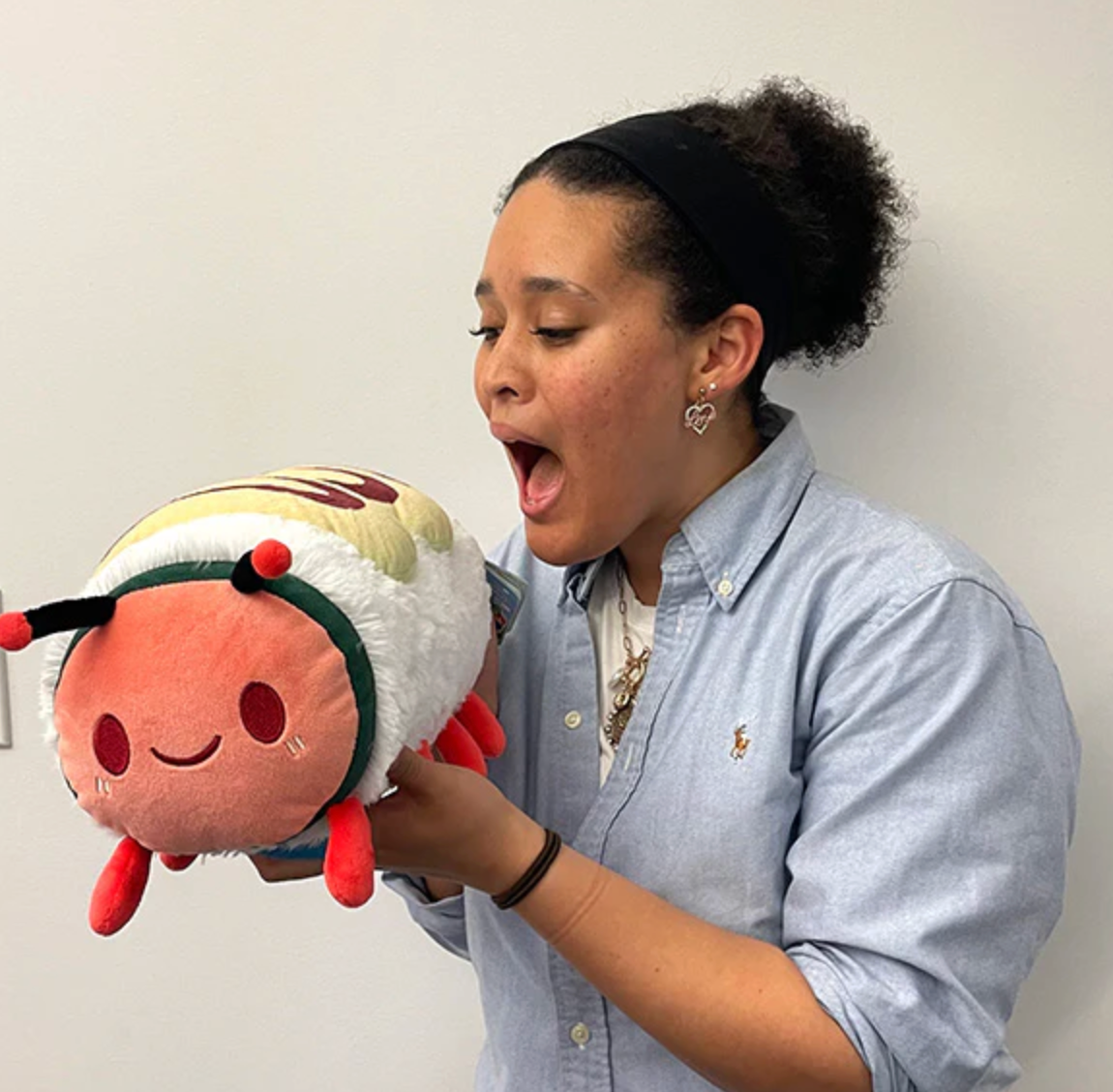 Person holding and looking excitedly at a plush toy of the Caterpillar Roll Mini sushi roll.