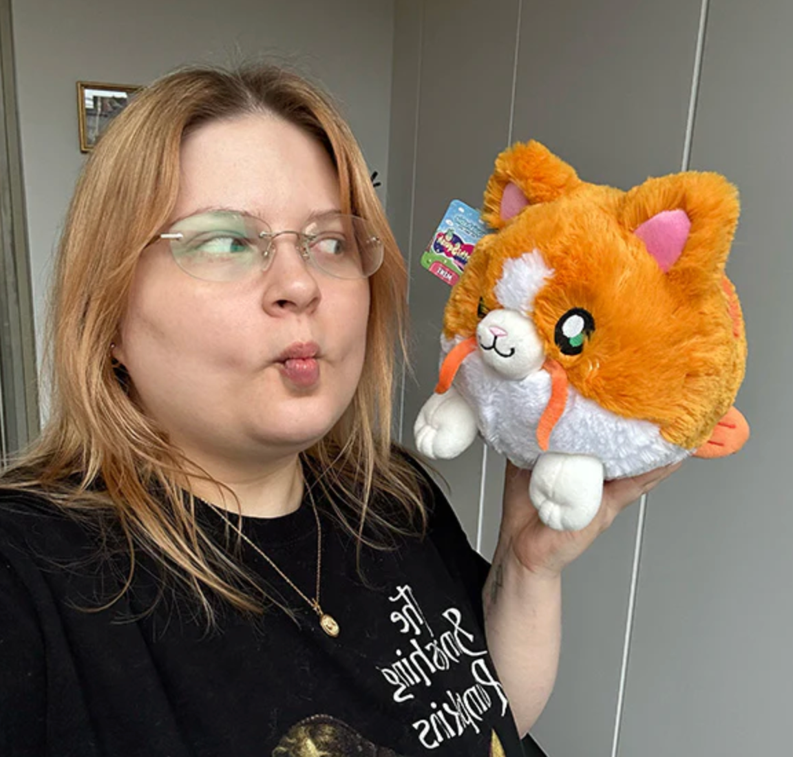 Person holding an orange and white plush toy Catfish Mini with cat and fish features, looking playfully at it.
