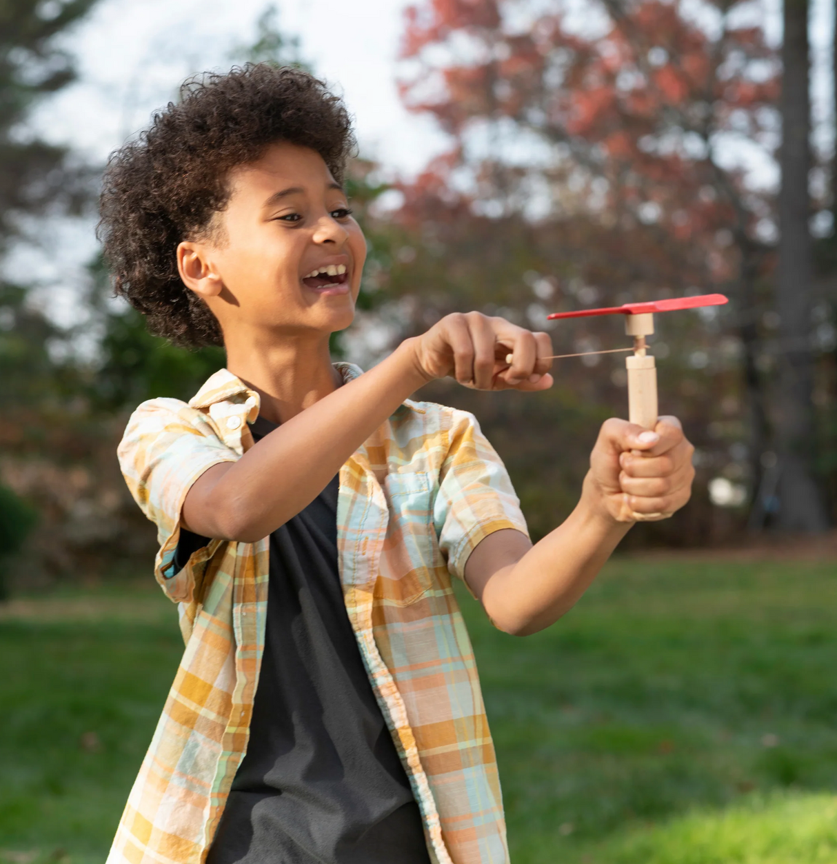 Child outdoors playing with a Huckleberry Pull Helicopter, winding the launcher and ready to take off with a smile.