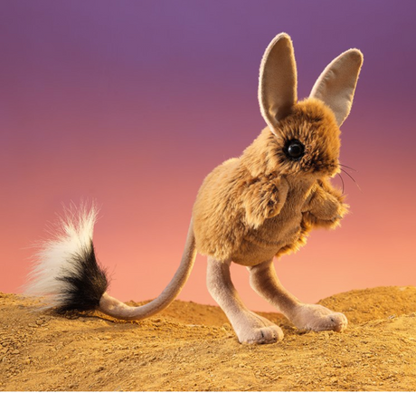 Jerboa Puppet with oversized ears and long tail standing on sandy ground against a colorful sunset backdrop.
