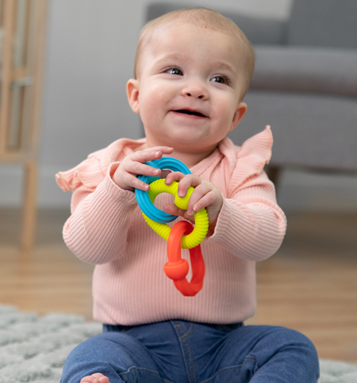 Baby holding colorful Plip Grips silicone links with textured surfaces for sensory play and fine motor skill development.