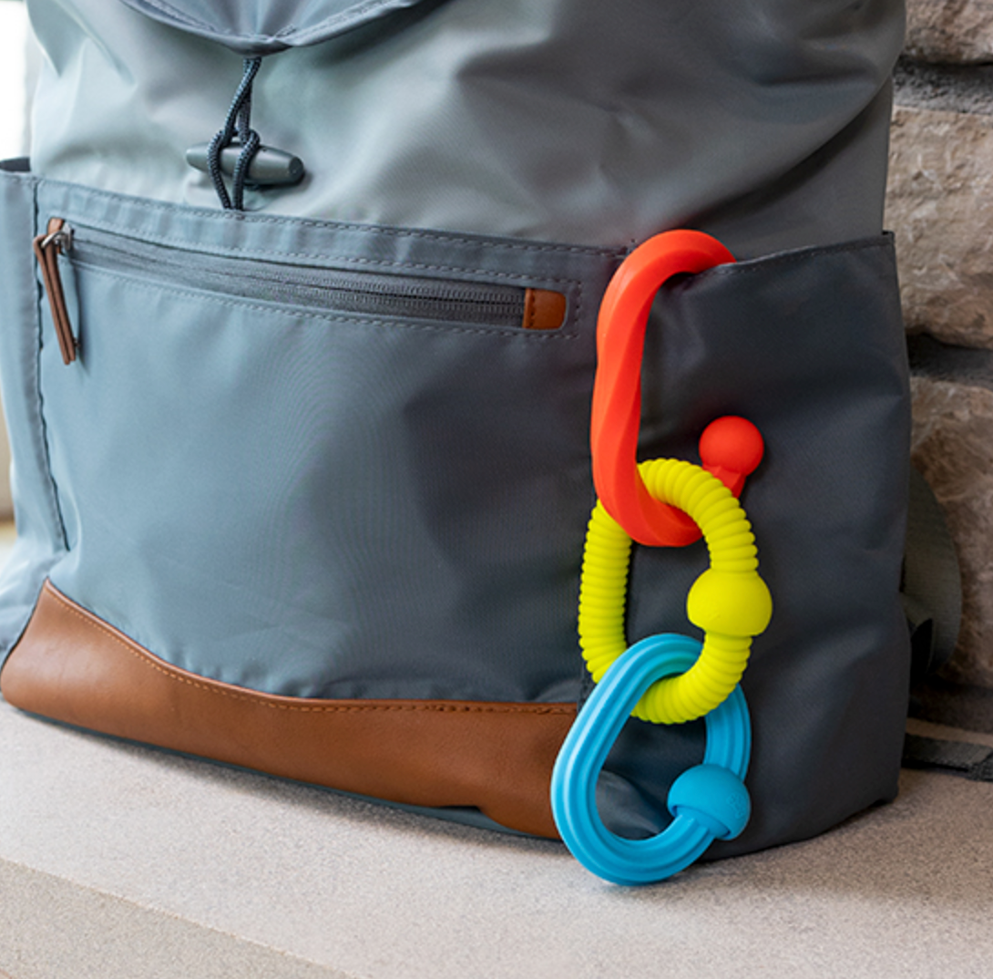 Plip Grips three colorful silicone links clipped to a gray backpack, perfect for sensory play and fine motor skills.