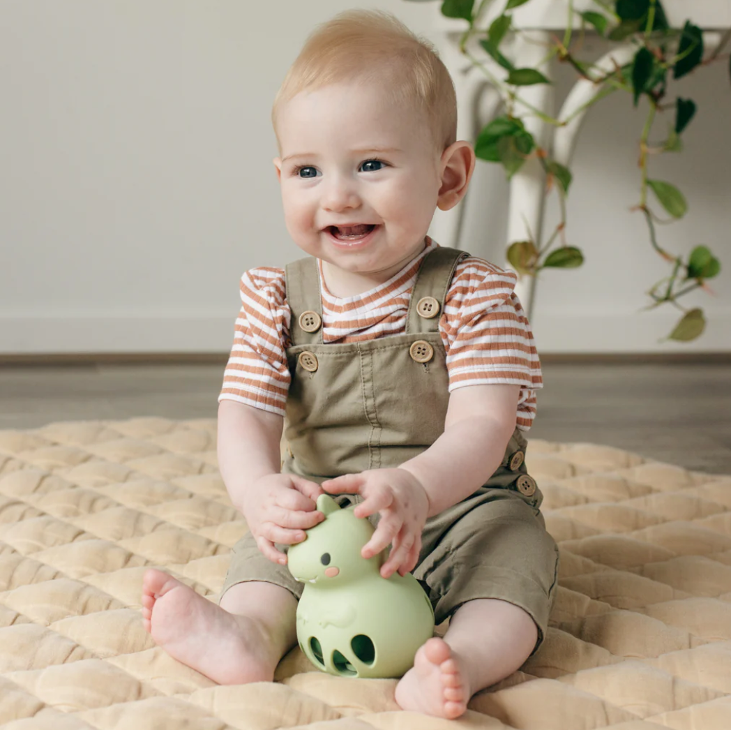 Baby smiling and holding the Silicone Rattle | Dino made of soft, safe silicone for sensory play and motor skill development.