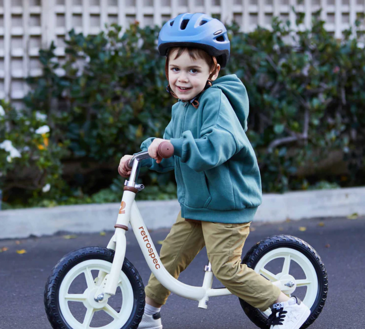 Child wearing a helmet riding a white Cub Balance Bike | Navy on a sidewalk, smiling and enjoying the ride.