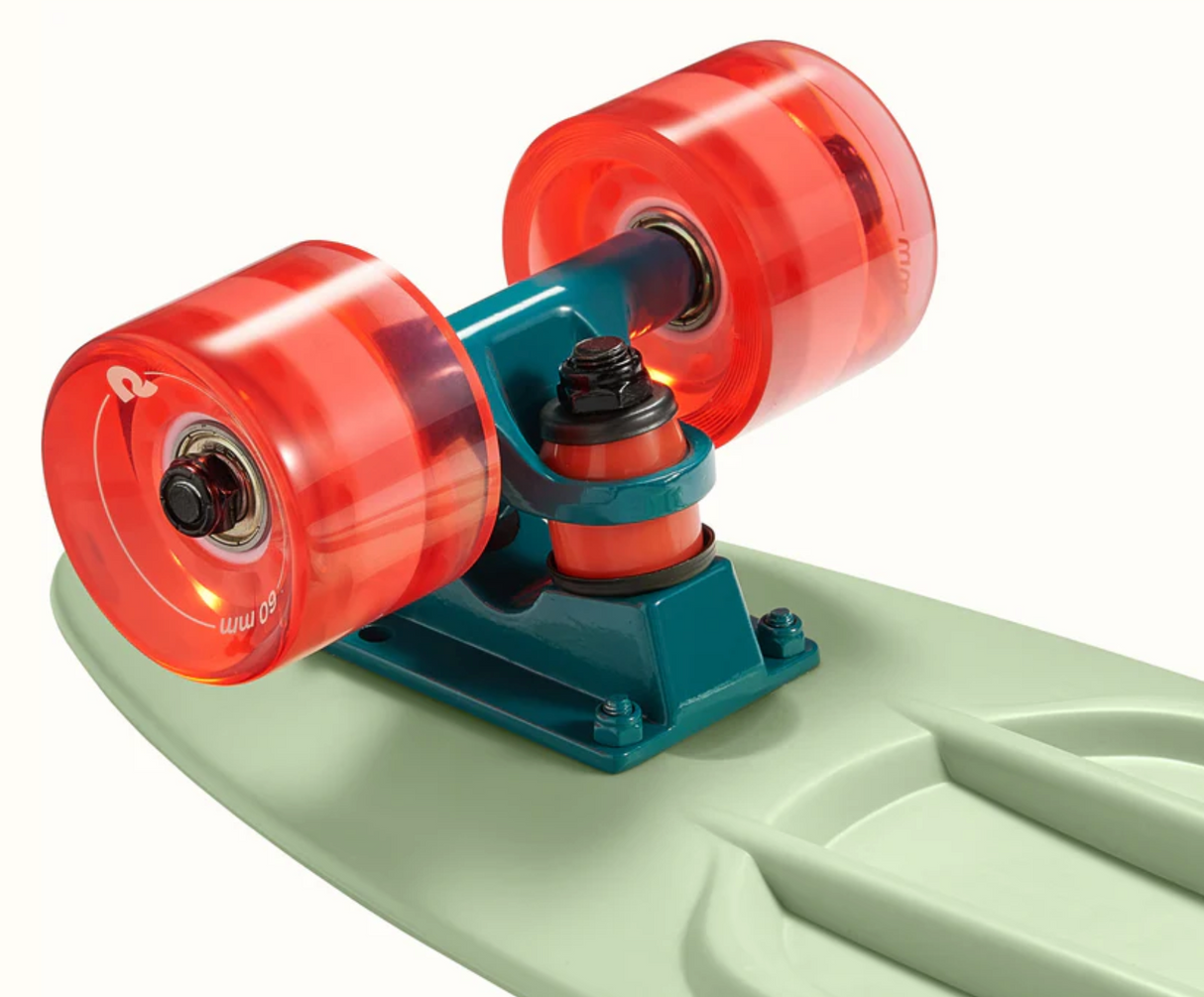 Close-up of the Quip Mini Cruiser Skateboard | Green Tea showing teal trucks and translucent orange wheels.