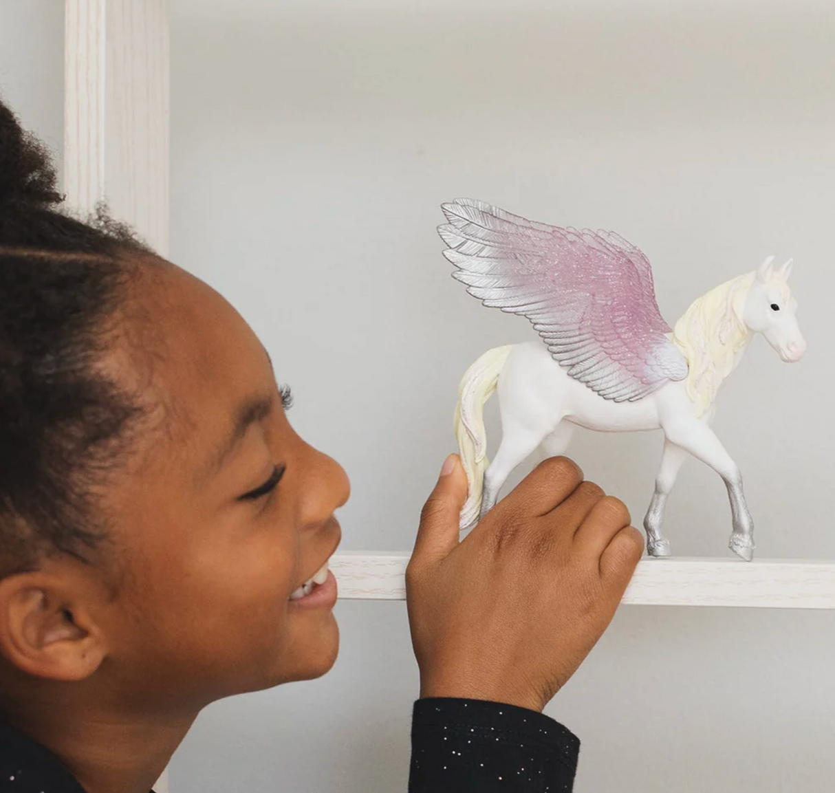 Child playing with the Bayala | Sunrise Pegasus figurine featuring glittering pink and silver wings on a white unicorn.