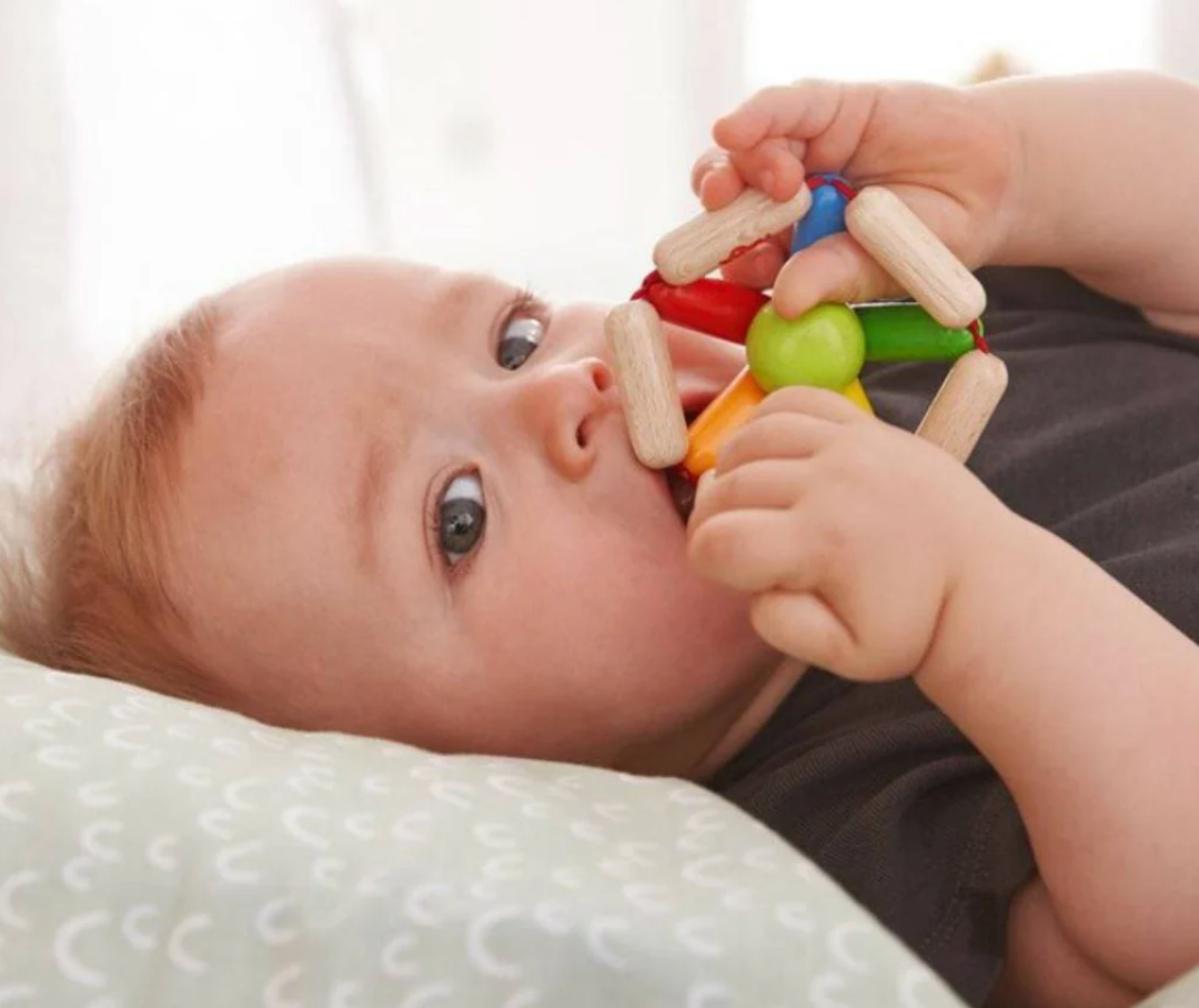 Baby holding and exploring the Color Carousel Wooden Rattle with vibrant colors and natural wood texture.
