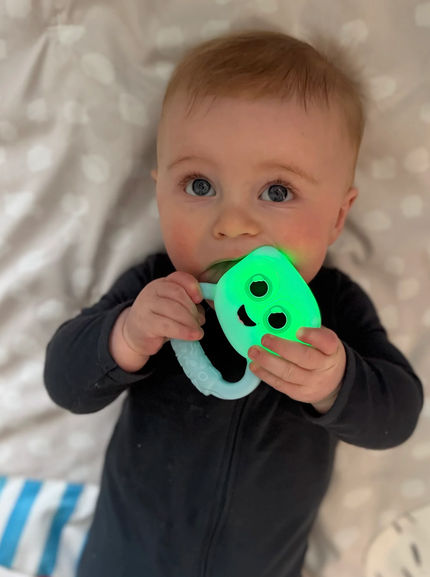 Baby holding and mouthing a glowing green Glo Pals Light Up Rattle | Blue with an easy-grip handle for sensory play.
