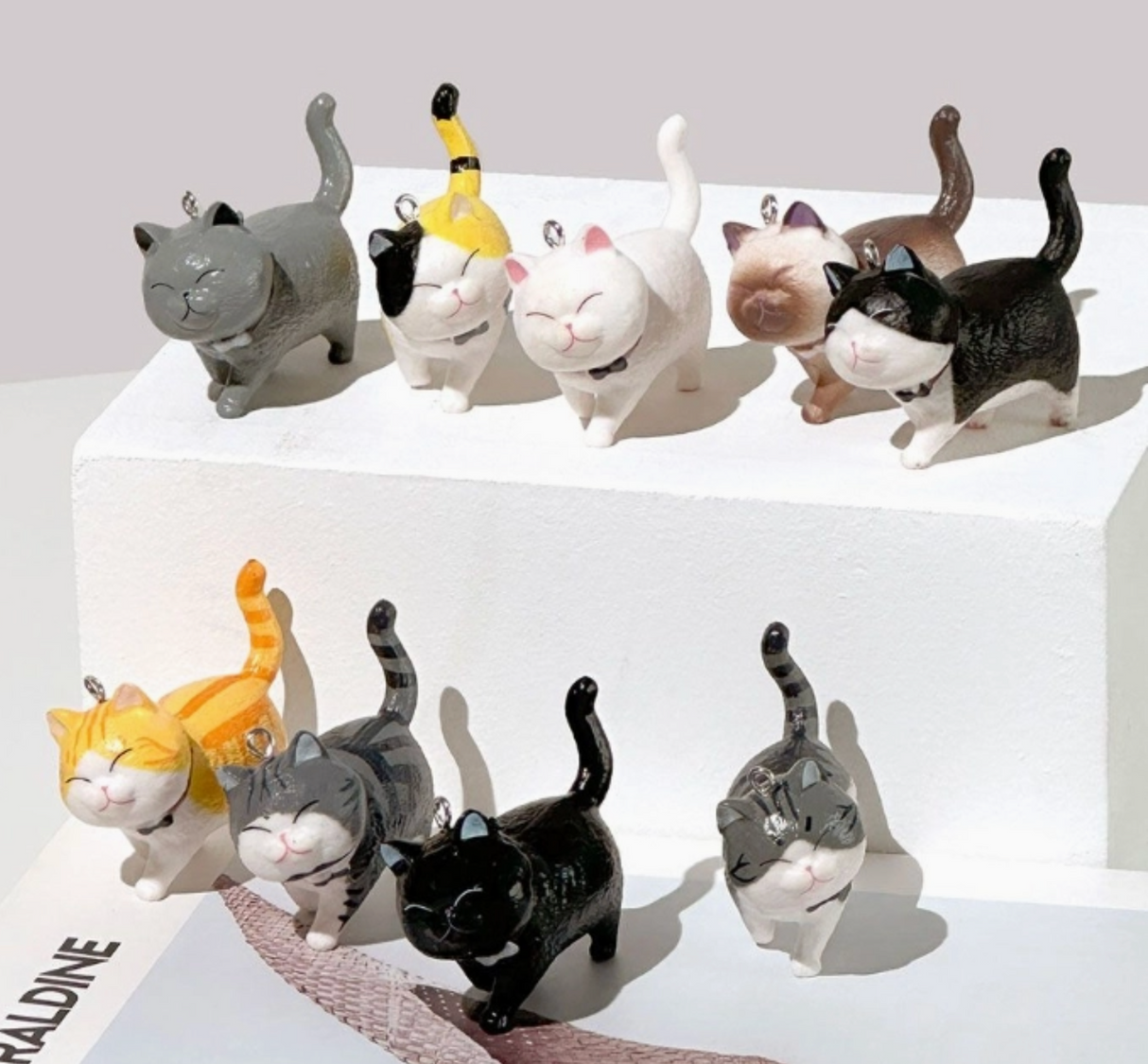Collection of cute cat keyrings with various colors and expressions displayed on white platforms