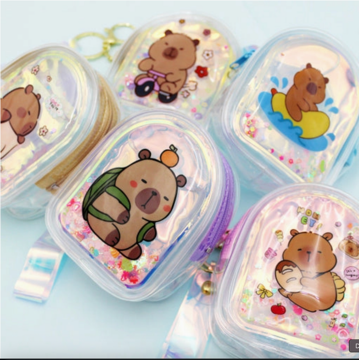 Holographic mini pouch keychains with cute capybara designs and floating glitter inside clear cases.