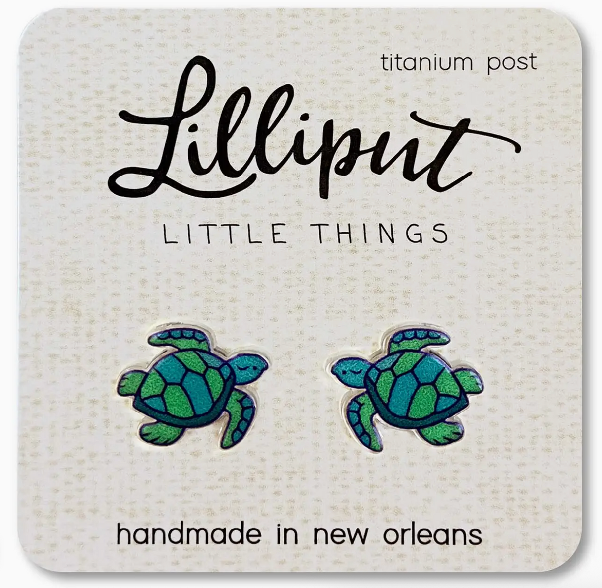Pair of handmade sea turtle stud earrings in green and blue shades with titanium posts on a branded card