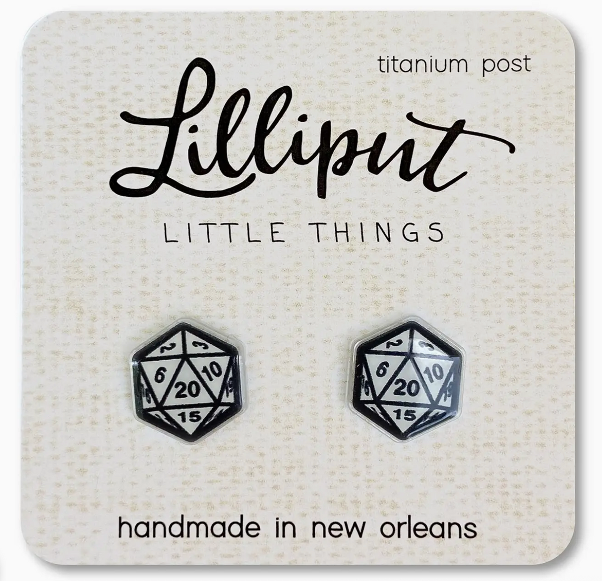 Pair of handmade black and white d20 dice stud earrings displayed on a branded card with titanium posts