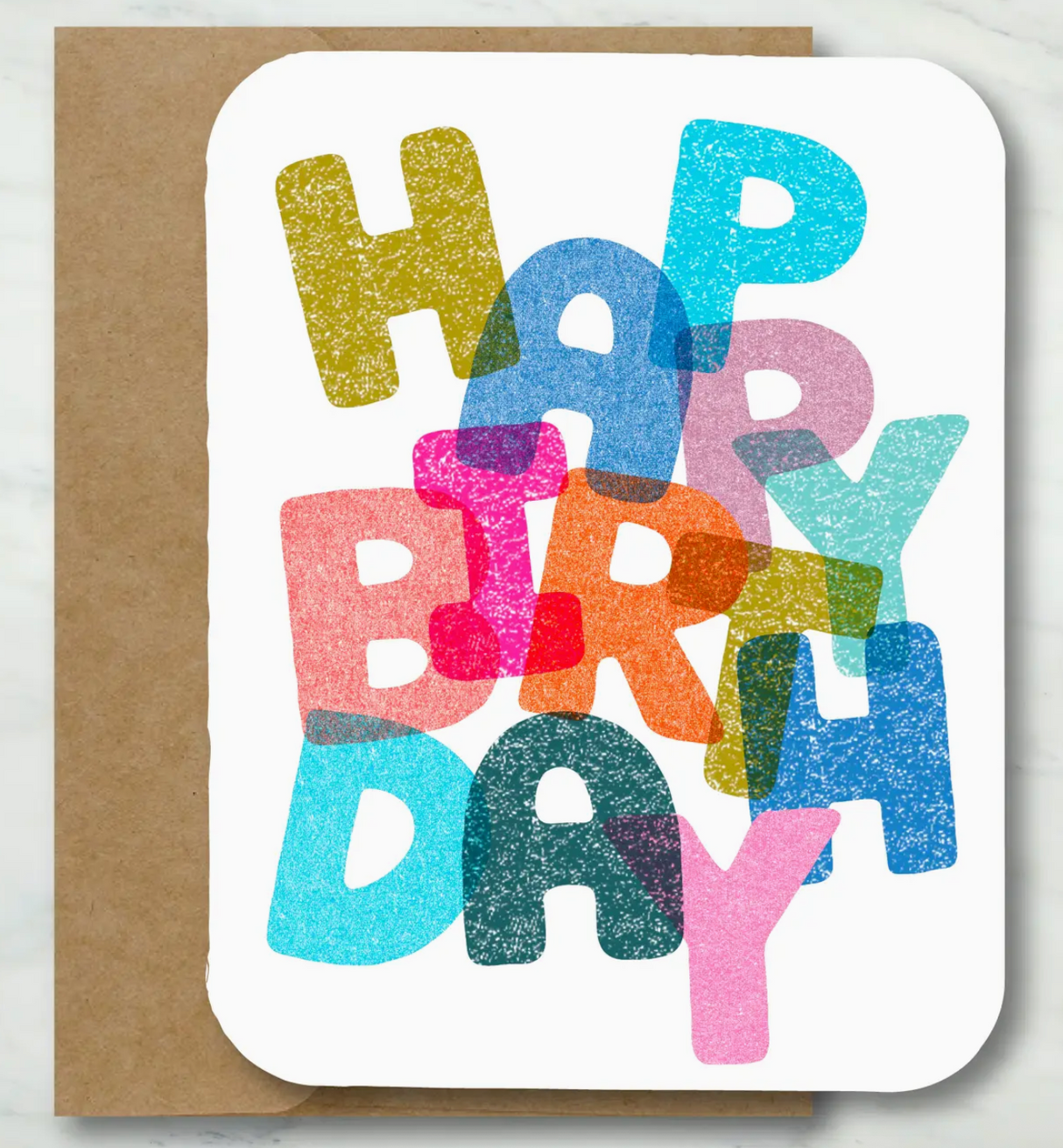 Colorful overlapping letters spell out Happy Birthday on textured white card with recycled kraft envelope behind it