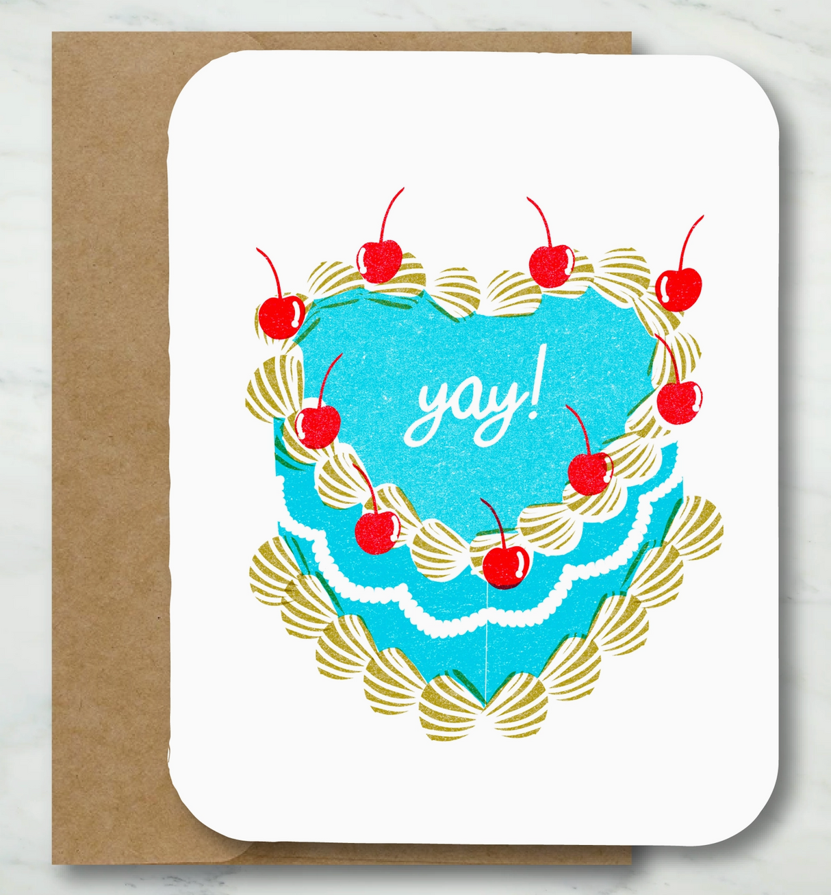 Folded card with blue heart-shaped cake, red cherries, and yay! text on white textured cardstock with kraft envelope.