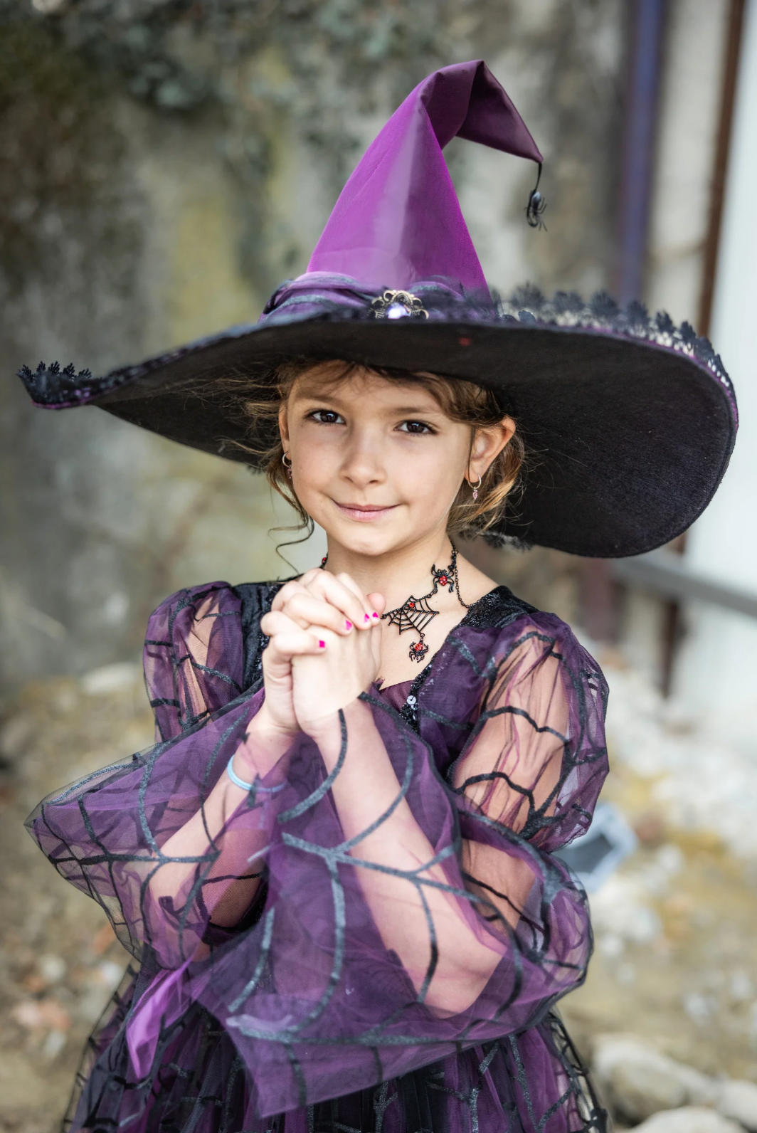 Young girl wearing an amethyst spider witch hat with lace trim and a playful spider detail at the tip