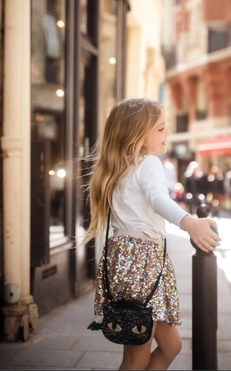 Young girl wearing a black glitter cat-shaped purse with embroidered eyes and whiskers on a city street