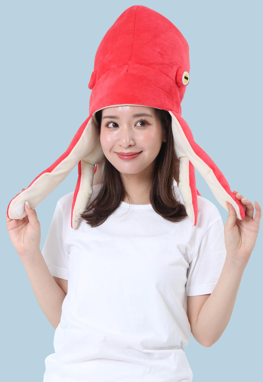 Person wearing a bright red soft octopus hat with long tentacles and playful eyes on light blue background