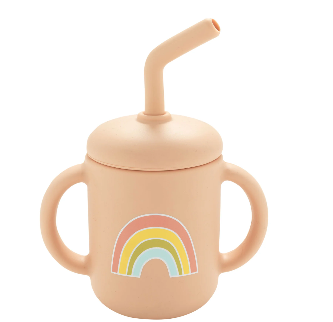 Silicone sippy cup in soft pink with two handles and a colorful rainbow design on the front with a removable straw lid.