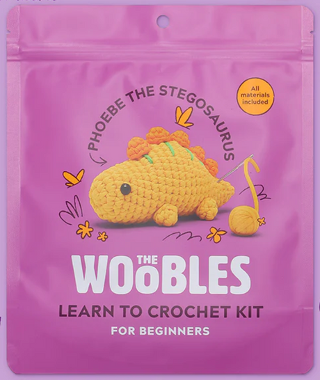 Phoebe the Stegosaurus crochet kit packaging in bright purple with a cute yellow crocheted dinosaur shown on the front