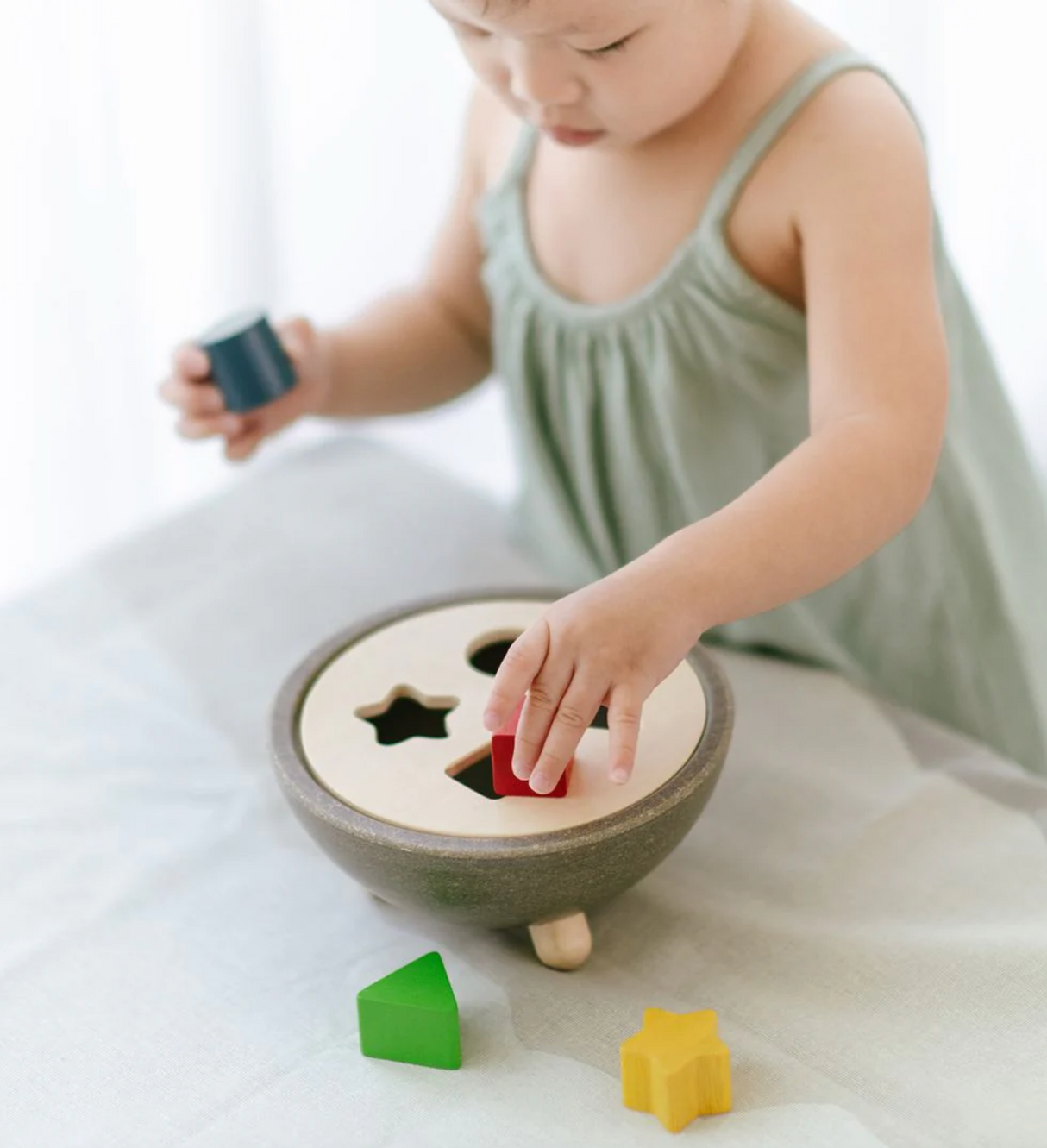 Toddler playing with a shape sorting bowl, matching colorful geometric pieces to their corresponding holes.