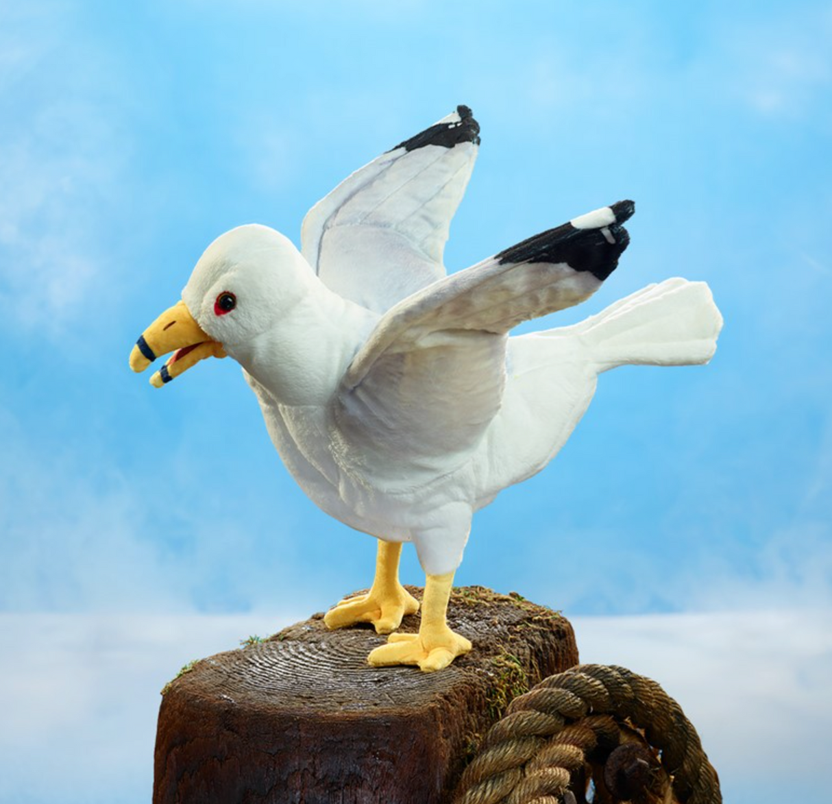 White and gray seagull puppet with movable beak and wings perched on wooden post against blue sky