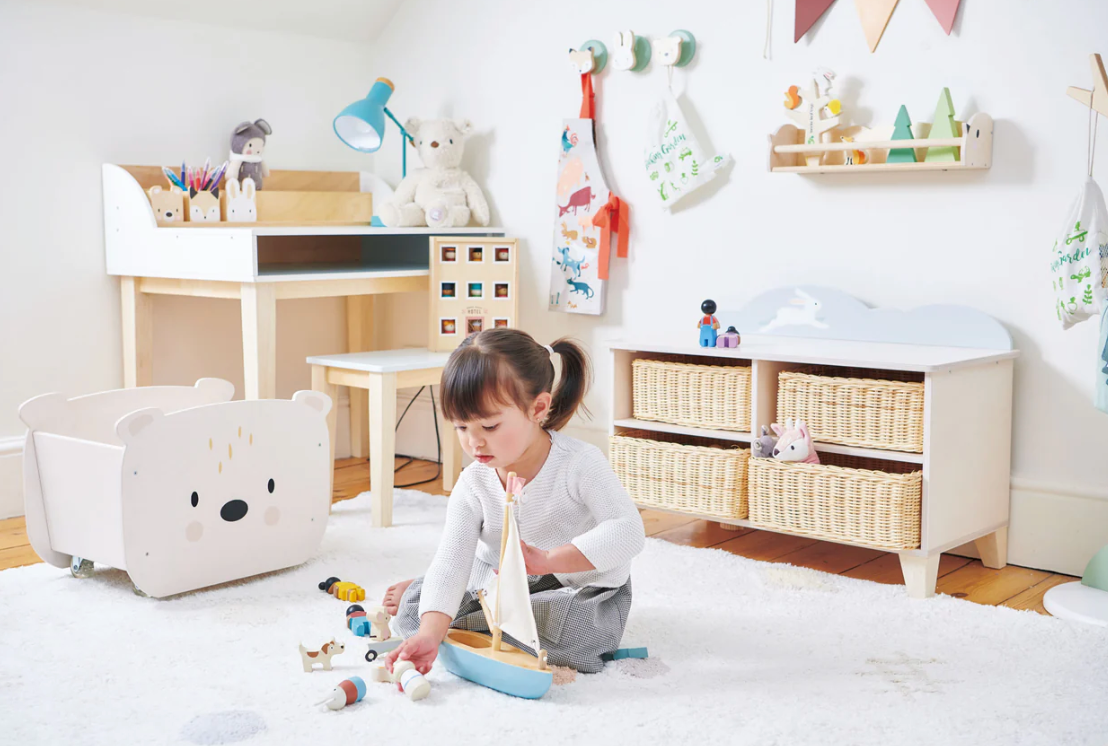Young child playing with a solid wood Sailaway Boat toy with fabric sails on a bright carpeted floor in a cozy room