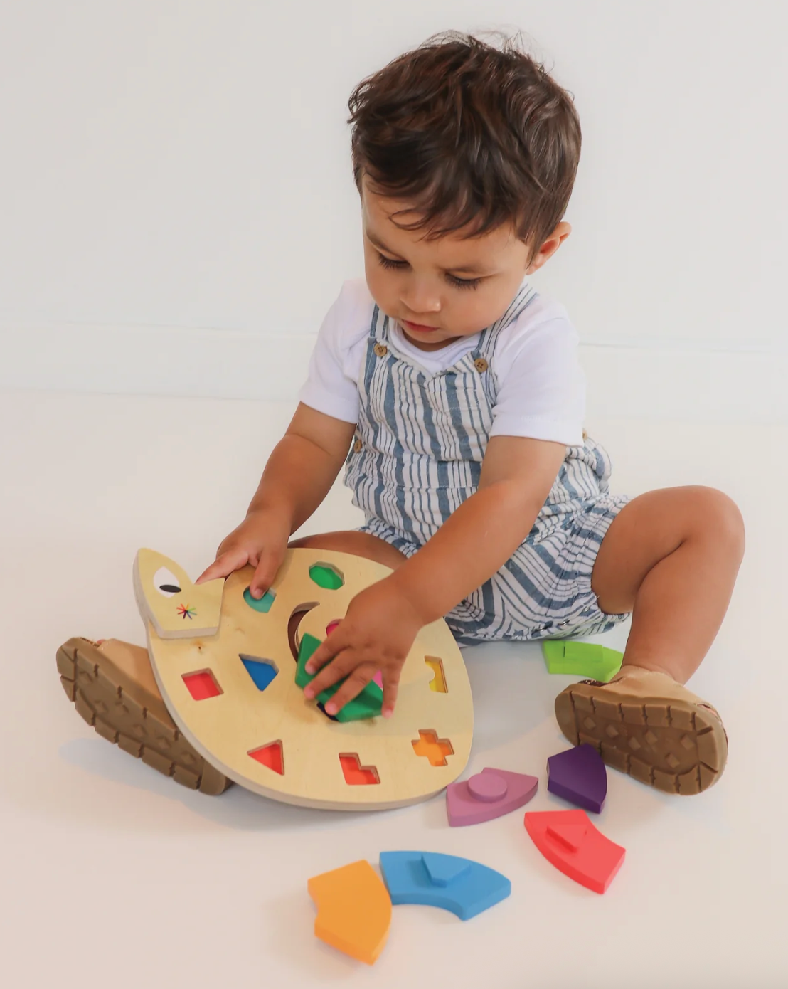 Toddler playing with a colorful wooden shape matching puzzle designed to fit into a 3D snake base.