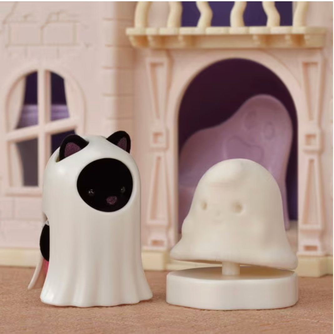 Small toy figure dressed as a ghost standing next to a ghost-shaped pedestal in front of a toy house.