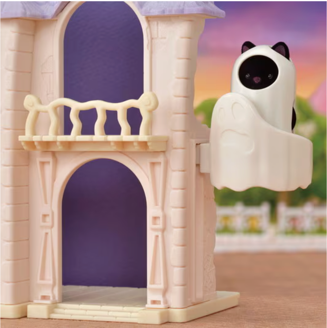 Small spooky house toy with a black cat figure dressed as a ghost floating beside the building at dusk.