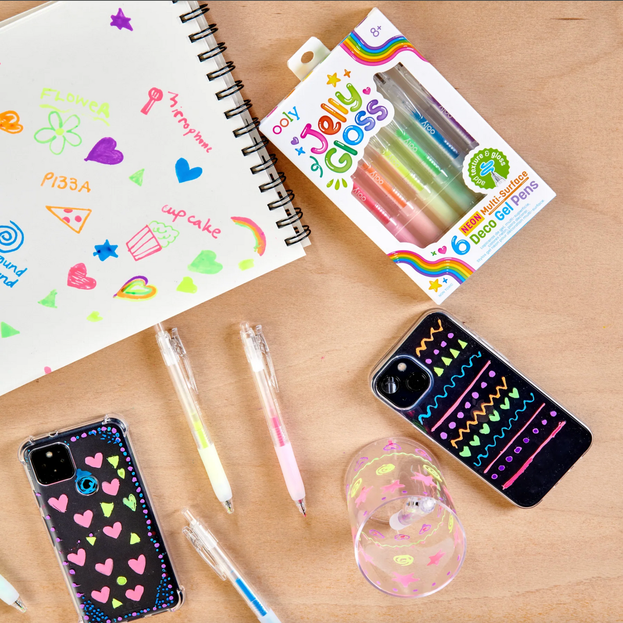 Set of six colorful Jelly Gloss multi-surface gel pens with craft designs on paper, phone cases, and glass jars.