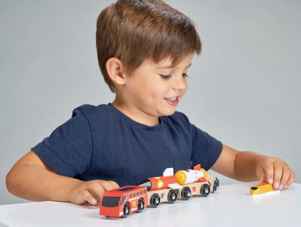 Young boy happily playing with a colorful wooden space rocket train set on a white table