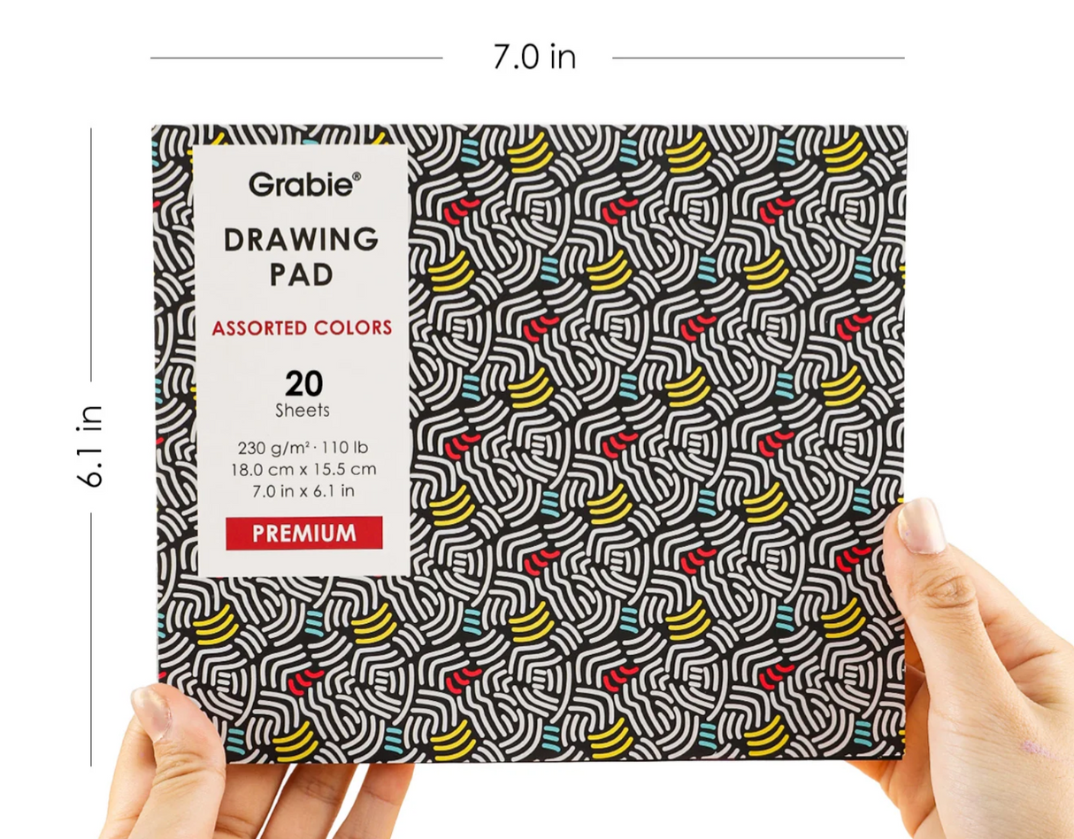 Hands holding a 7x6 inch Grabie drawing pad with 20 assorted color sheets and a colorful abstract cover design