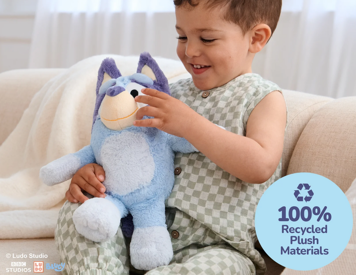 Young child smiling and playing with a soft blue plush toy inspired by the Australian Bluey character