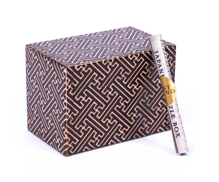 Intricately designed Japanese puzzle box with geometric patterns and a rolled instruction paper on a white background