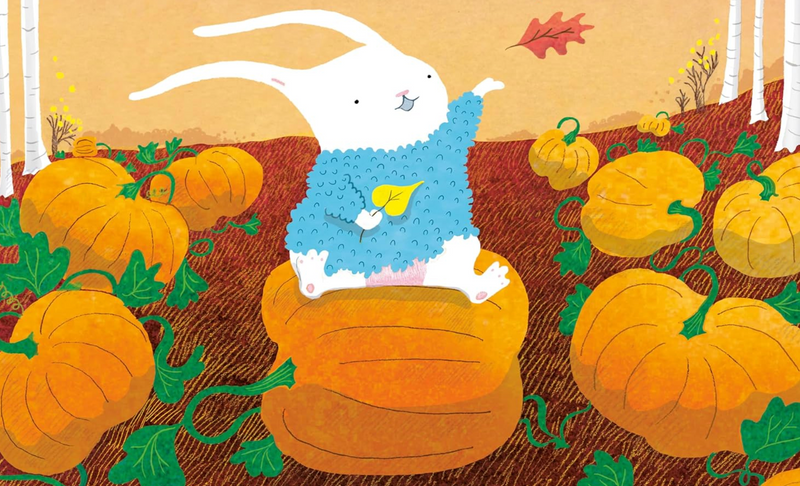 A playful white rabbit wearing a blue sweater sitting on a large pumpkin in an autumn pumpkin patch.